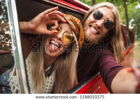 Photo of caucasian hippie couple smiling and fooling around while driving retro minivan in forest