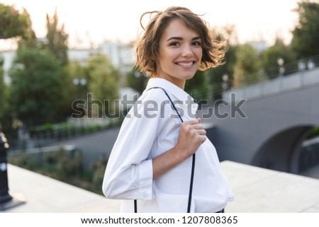 Smiling young woman walking outdoors, looking at camera