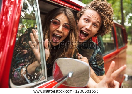 Photo of amusing hippie couple smiling and fooling around while driving retro minivan in forest