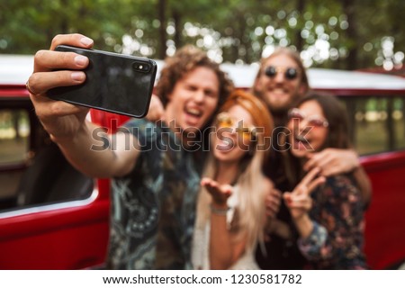 Group of european hipsters men and women smiling and taking selfie on mobile phone near vintage minivan into the nature