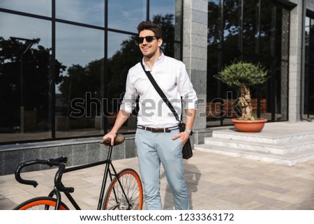 Handsome young business man dressed white shirt walking outdoors with bicycle