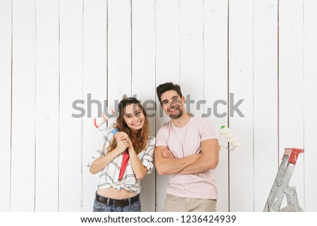 Photo of smiling couple man and woman painting white wall and making renovation using paint rollers