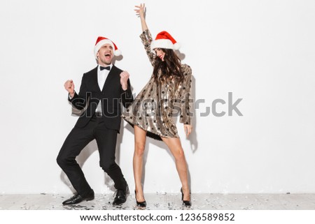Cheerful young smartly dressed couple wearing red hats celebrating New Year party isolated over white background