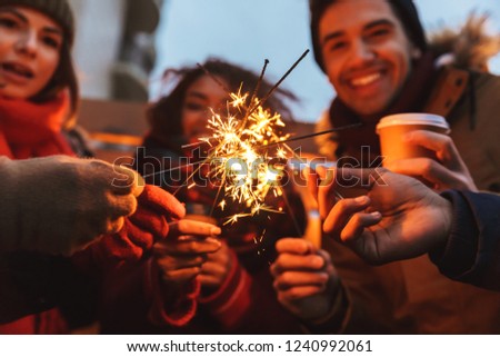 Image of a happy young friends talking with each other drinking coffee outdoors winter concept holding bengal lights.