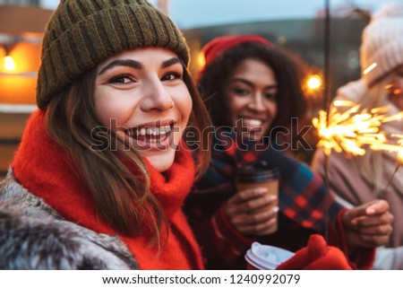 Image of a happy young friends talking with each other drinking coffee outdoors winter concept holding bengal lights.