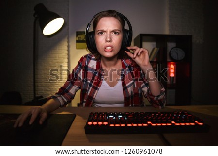 Shocked girl gamer sitting at the table, playing online games on a computer indoors