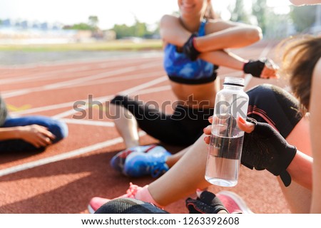 Group of motivated sports people warming up on track, doing exercises, drinking water