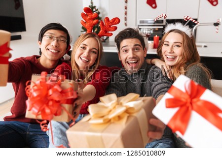 Group of happy young friends celebrating New Year together while sitting on a sofa at home, giving presents