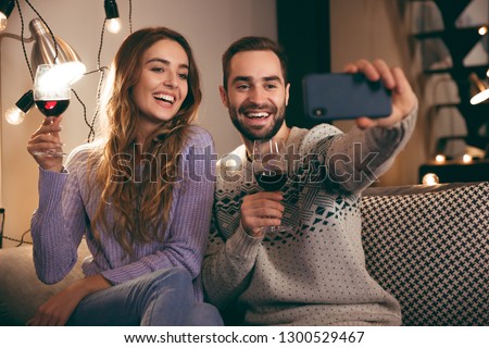 Beautiful happy young couple spending romantic evening together at home, drinking red wine, taking a selfie
