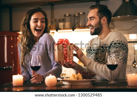 Beautiful happy young couple spending romantic evening together at home, drinking red wine, man giving a present