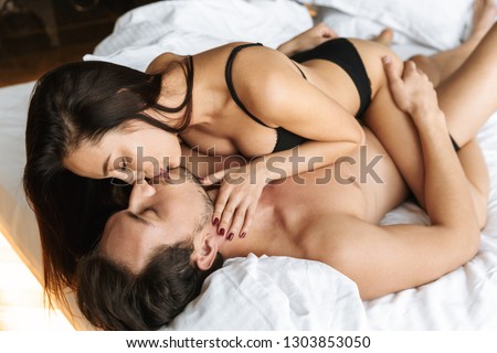 Image of a young loving couple indoors in home in bed lies hugging and kissing.