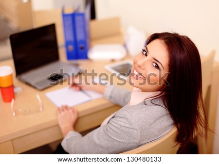 Young businesswoman sitting at desk and working. Smiling and looking back at camera