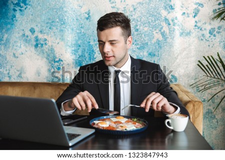 Image of a handsome young businessman sitting in cafe using laptop computer have a breakfast or dinner eat.