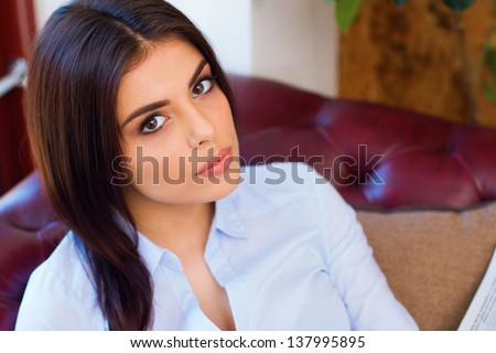 Portrait of a young beautiful woman sitting on the sofa and looking to the camera