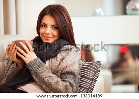Happy young woman sitting on sofa in cozy cloths with cup of coffee