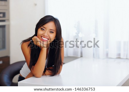 Happy beautiful asian woman leaning on hand in her kitchen