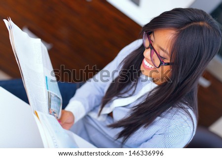 Young happy asian businesswoman reading newspaper