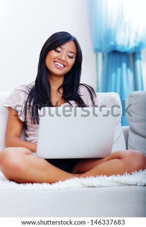 Happy young asian woman with her laptop at home sitting on sofa