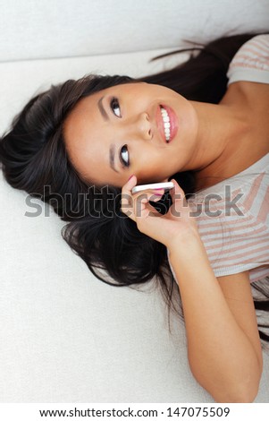 Happy asian woman lying on sofa while talking on phone