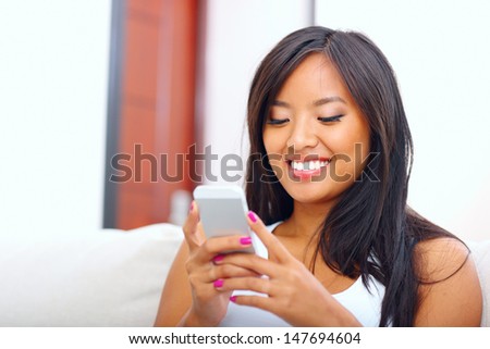 Beautiful young asian woman text messaging with her smart phone at home
