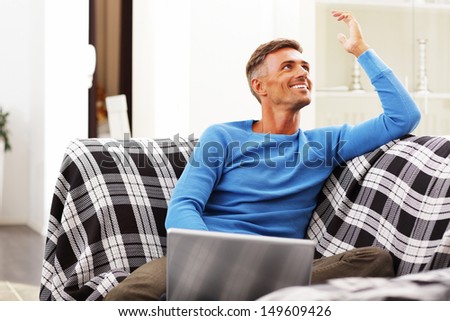 Handsome young man using laptop at home, sitting in armchair, smiling.