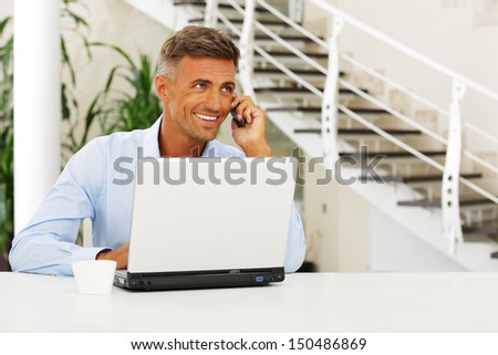 Mature happy man on phone sitting at the desk