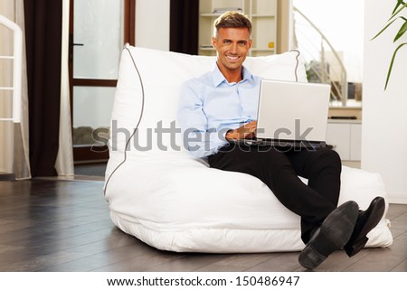 Handsome confident man sitting in armchair with laptop at home