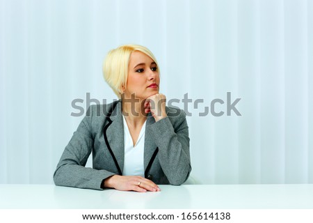 Beutiful thoughtful businesswoman sitting at the table and looking left at copyspace in office