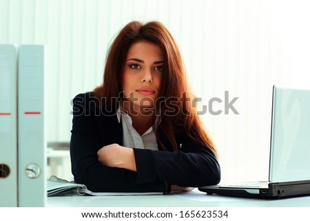 Young serious businesswoman sitting at the table in office