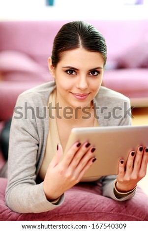 Young beautiful woman lying on the couch and holding tablet computer at home