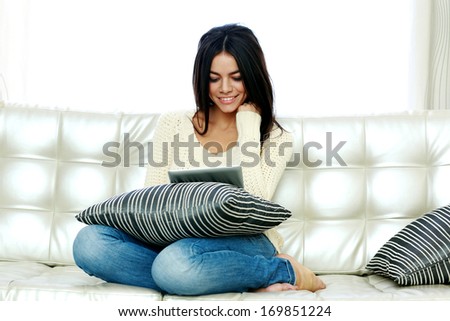 Portrait of a happy woman sitting on the sofa and using tablet computer