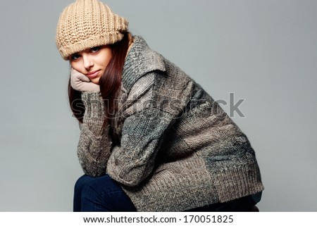 Young thoughtful woman in warm winter outfit on gray background