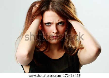 Young angry woman touching her head on gray background