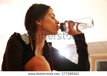 Young fit woman drinking water at gym