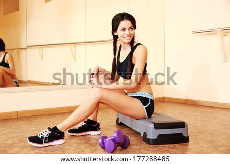Young smiling fit woman sitting on the step board at gym