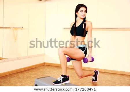 Young happy fit woman doing exercises with dumbells on step board at gym
