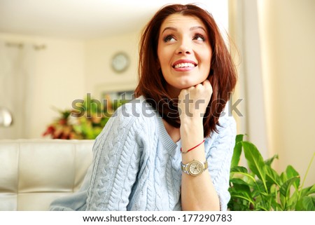 Smiling thoughtful woman looking up at home