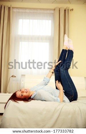 Happy woman lying on the bed with raised legs at home