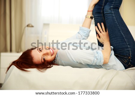 Cheerful woman lying on the bed with raised legs at home