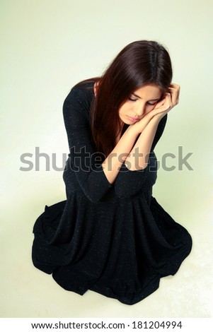 Studio shot of a beautiful sad woman in black dress sitting on the floor on gray background
