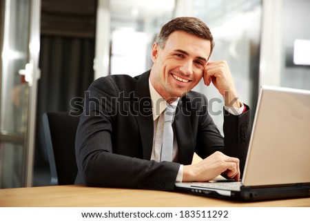 Smiling businessman sitting with laptop at office