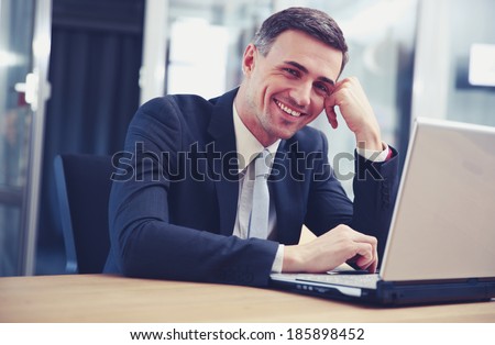 Cheerful businessman sitting with laptop at office