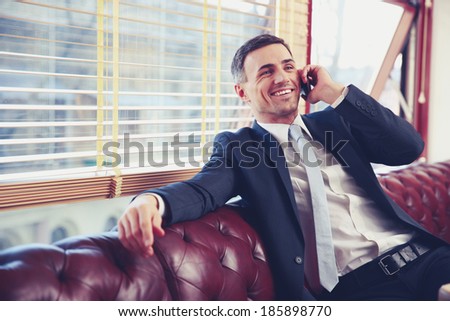 Happy businessman sitting and talking on the phone at office