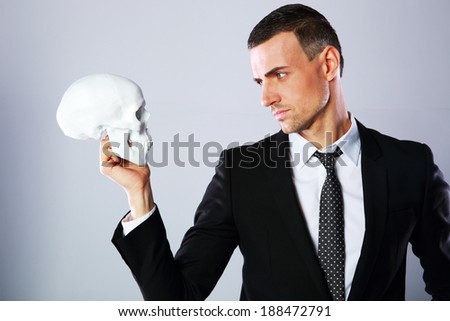 Businessman holding skull and looking on it over gray background