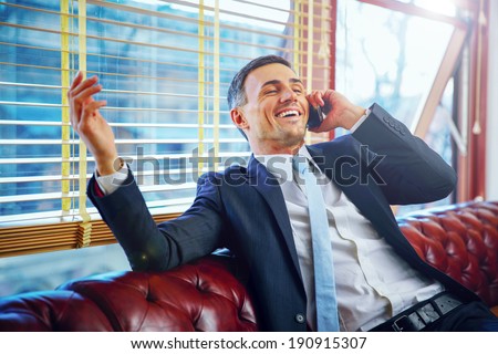 Laughing businessman sitting and talking on the phone at office