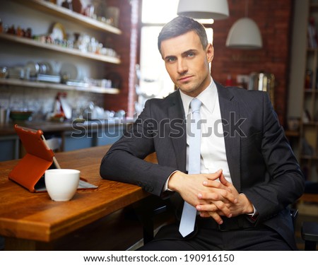 Confident businessman in formal cloths drinking coffee and reading news in the kitchen