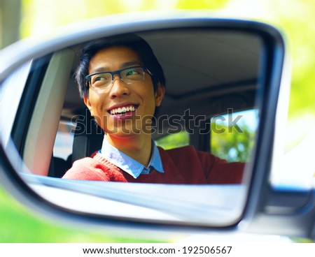 Smiling asian driver is reflected in mirror of car