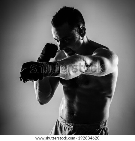 Naked sportsman boxing with his hands wrapped with elastic bandage on gray background
