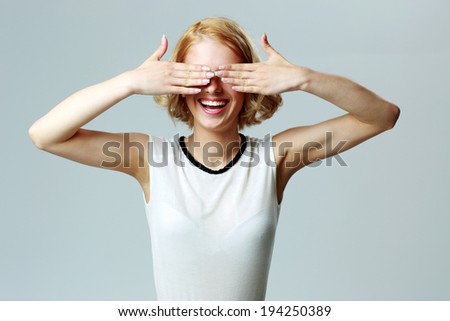 Portrait of a laughing woman closing her eyes with hands over gray background
