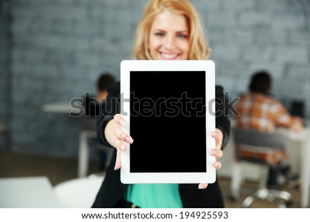 Young smiling woman showing blank tablet computer screen in office. Focus on tablet computer